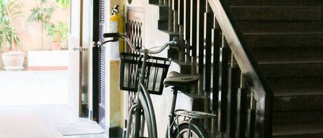 Una escalera con una bicicleta apoyada en la pared, una planta en maceta y una puerta que da a un espacio exterior con plantas.
