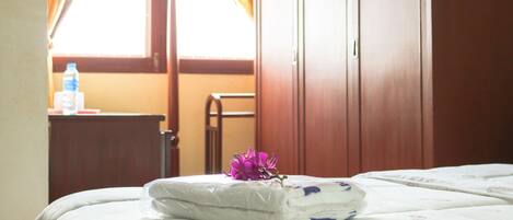 A hotel room with a neatly made bed, a wooden wardrobe, and a window with curtains.