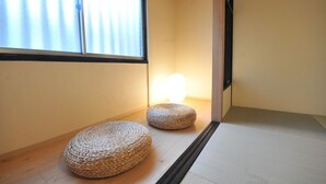 Ein Zimmer mit Tatami-Böden, zwei gewebten Tatami-Matten, einer Schiebetür und einem Fenster mit Jalousien.