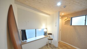 Une pièce avec un plafond en bois, une fenêtre donnant sur un beau paysage, une planche de surf appuyée contre le mur, une chaise et un porte-manteau suspendu.