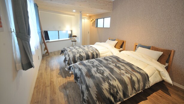 Une chambre d’hôtel avec deux lits, un plancher en bois, une fenêtre avec des rideaux, un bureau et une chaise.