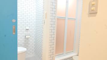 A narrow hallway with a blue door leading to a bathroom with white brick walls, a white toilet, and a window.