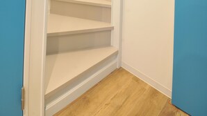 Un couloir étroit, avec un plancher en bois et une porte bleue sur le côté droit.