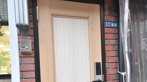 Une porte en bois avec un cadre noir, un petit appareil électronique fixé au mur et un objet blanc suspendu sur le côté droit.