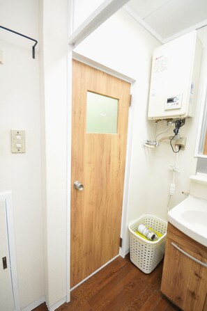 A bathroom with a wooden door, a white sink, a white laundry basket, and a white heater mounted on the wall. - Condominium House in Osaka Nakatsu (Osaka)