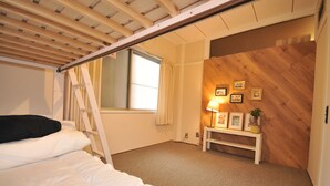Une chambre avec un lit en mezzanine, une fenêtre avec des rideaux, une table de chevet avec une lampe et un mur en bois orné de tableaux encadrés.