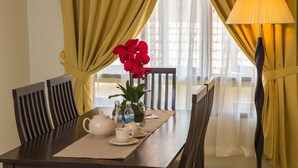 A dining table set with a teapot, cups, saucers, and a vase with red flowers.