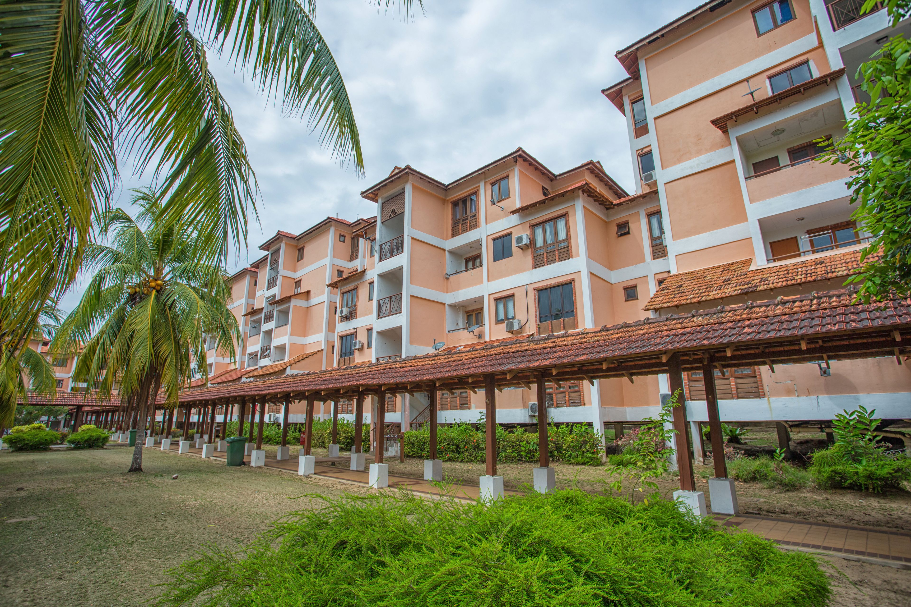 A multi-story hotel with balconies, a covered walkway, and palm trees.