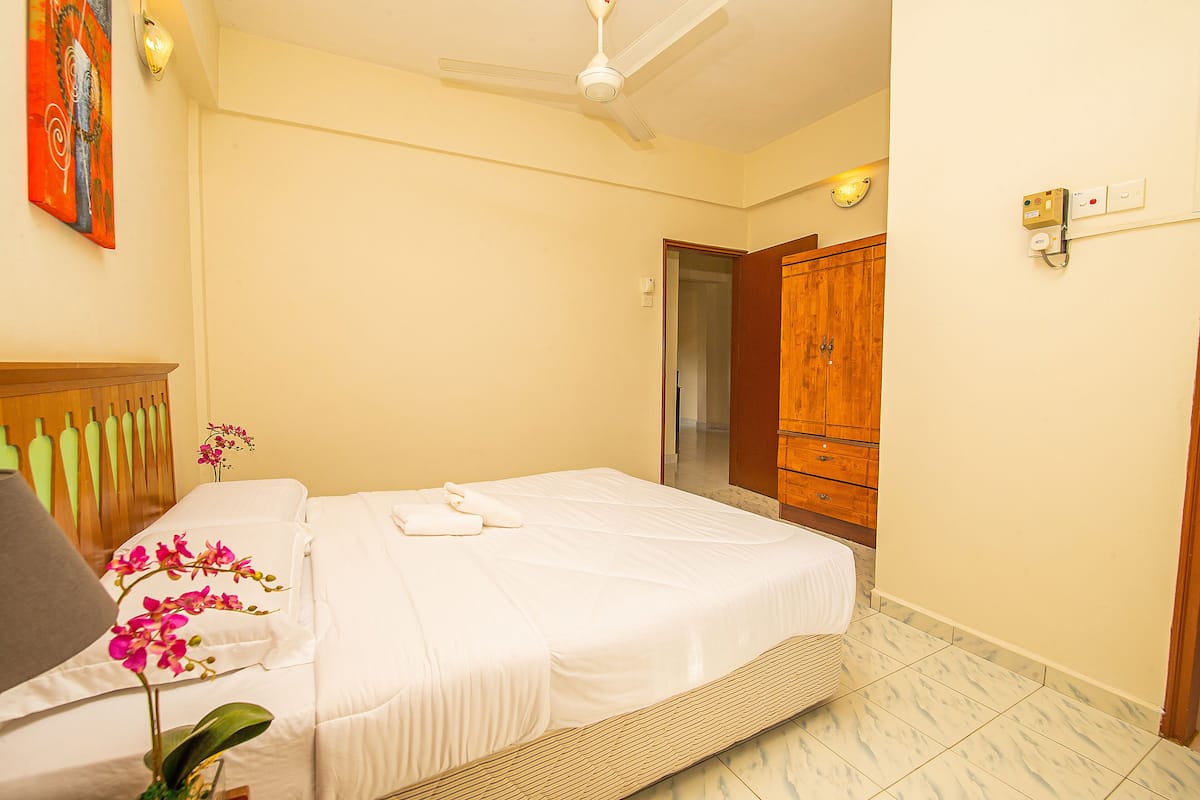 Une chambre à coucher comprenant un lit, une armoire en bois, un ventilateur de plafond et un luminaire fixé au mur.