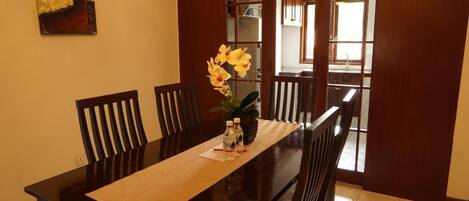 A dining area with a wooden table, chairs, and a vase with yellow flowers.