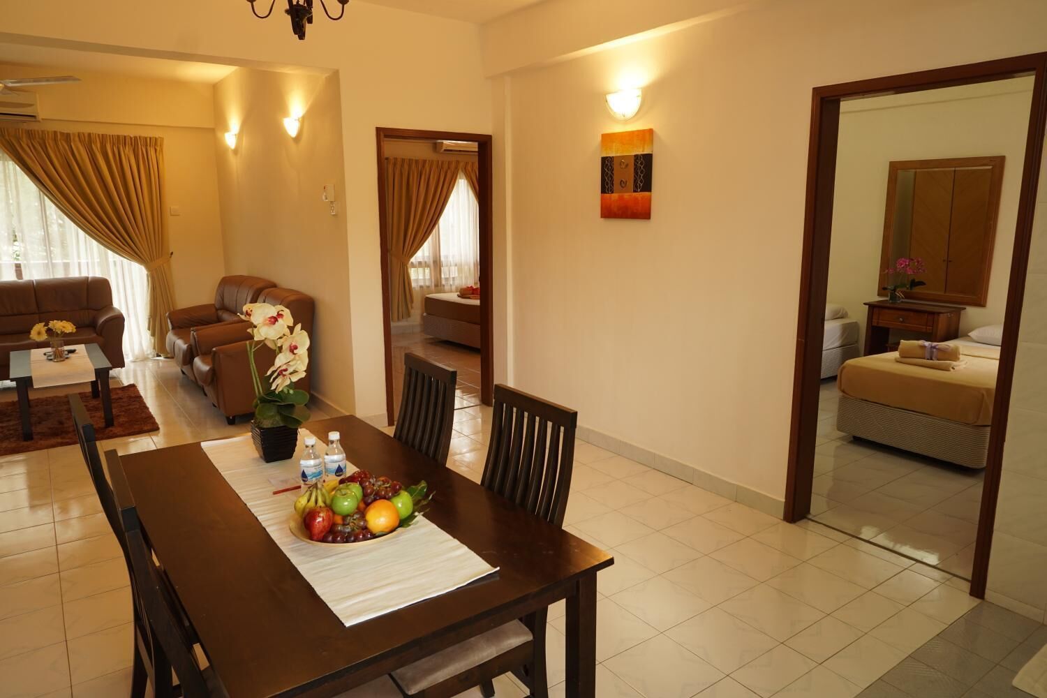 A dining area with a wooden table set for two, a brown leather sofa, and a potted orchid.
