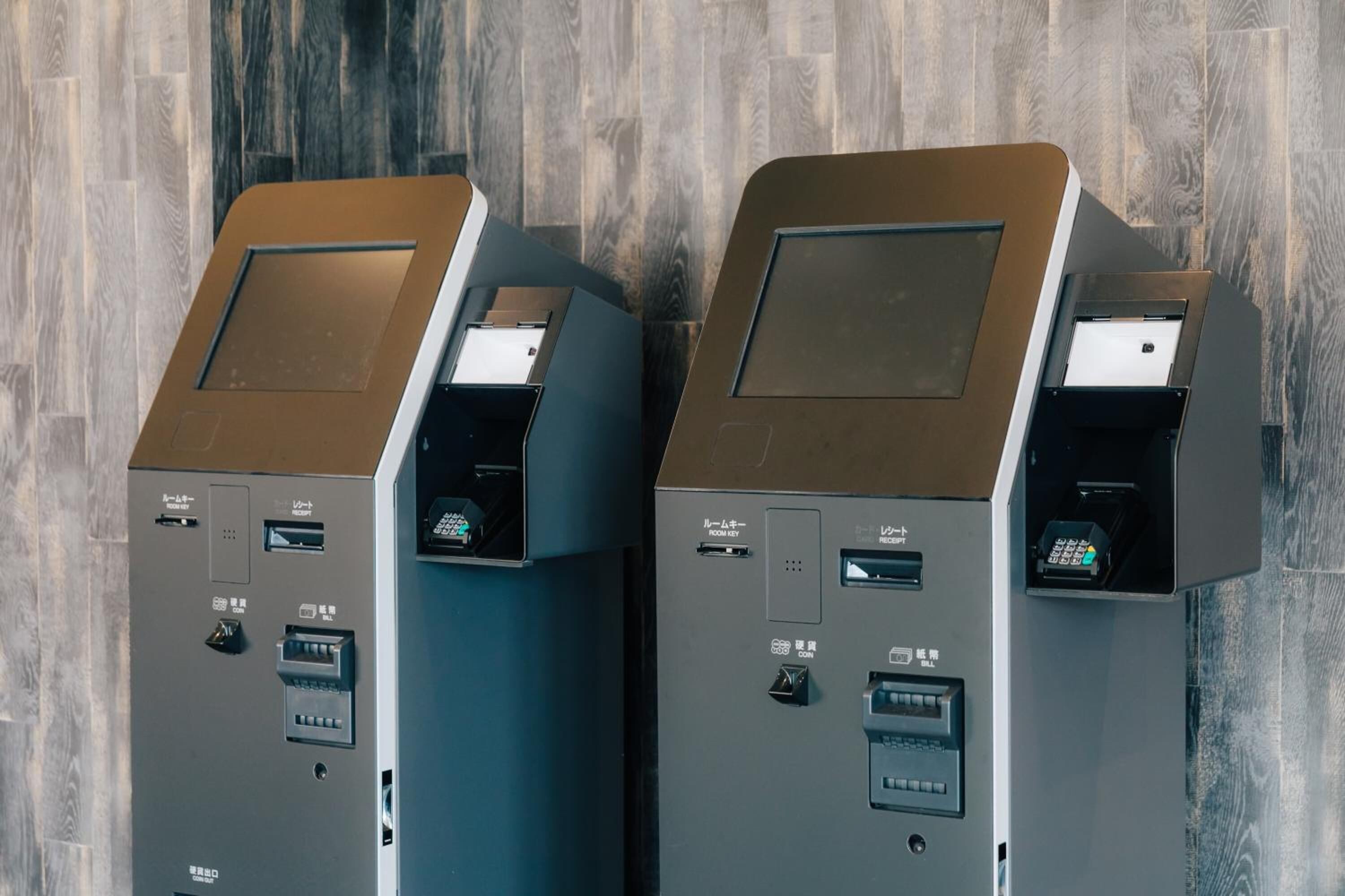 Three ATMs with card slots and cash withdrawal machines, set against a wooden floor background.