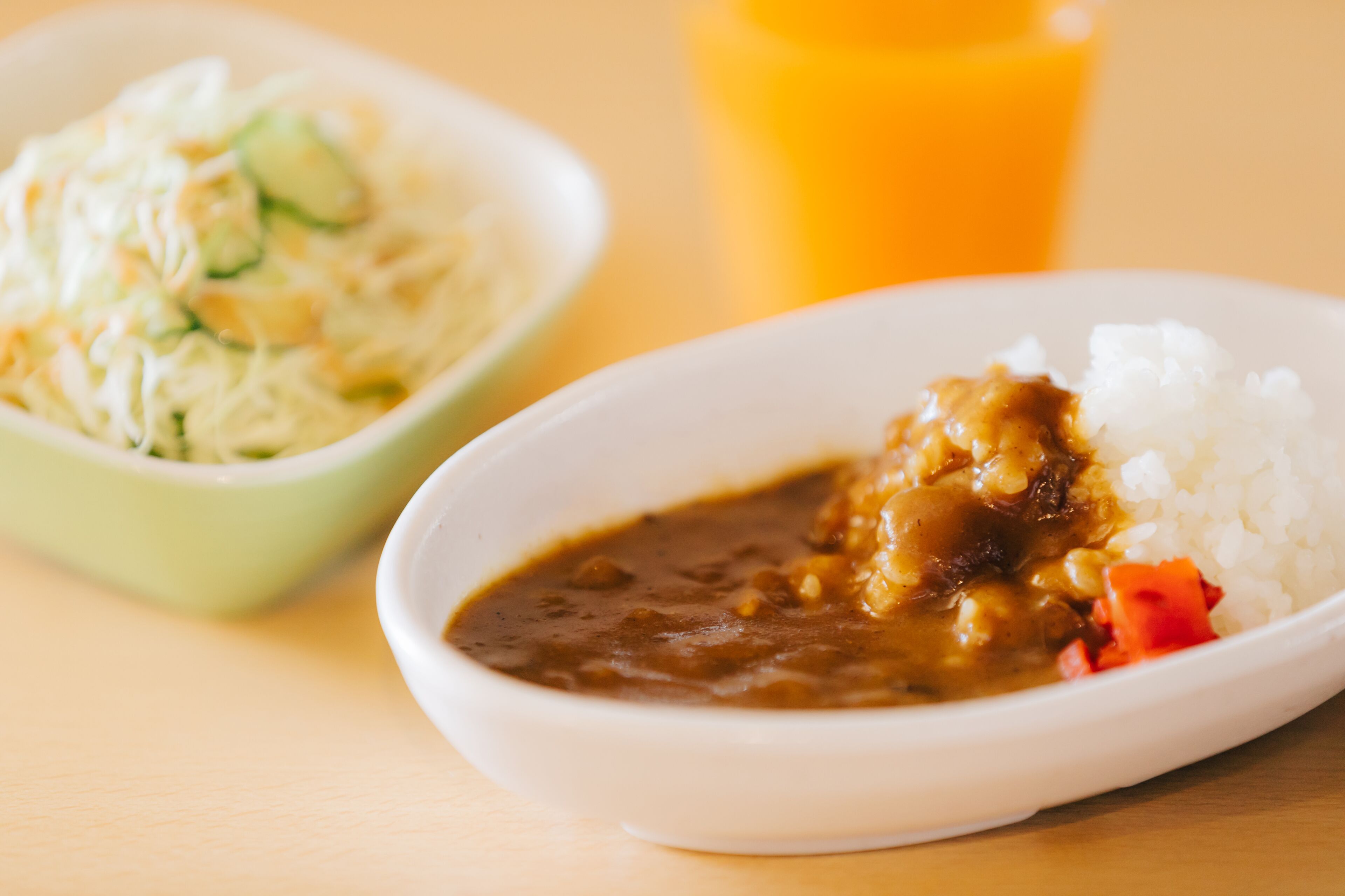 A plate of white rice with a brown sauce and vegetables, and a bowl of coleslaw with cucumbers and shredded cabbage.