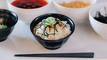 A bowl of rice topped with green onions and seaweed, surrounded by other bowls of food.