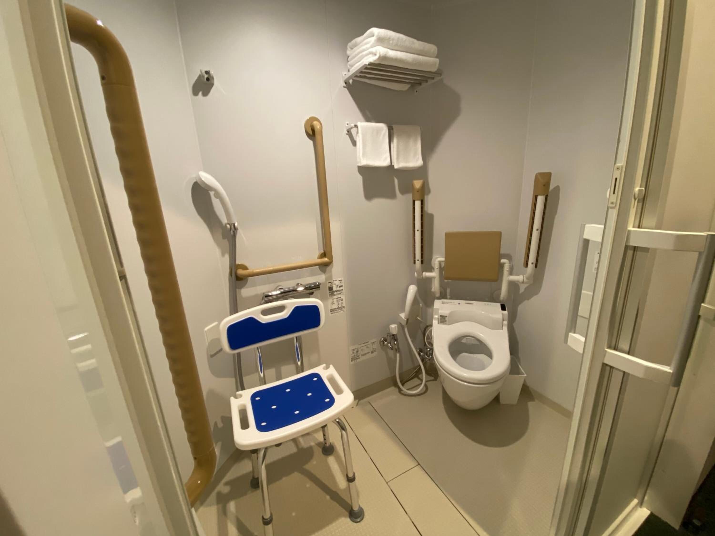 Un baño pequeño y privado con inodoro accesible para sillas de ruedas, asiento de ducha y barra de apoyo.