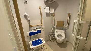 Een kleine, privé badkamer met een toilet aangepast voor rolstoelgebruik, een douchestoel en een handgreep.