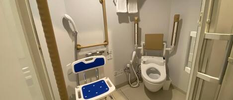 A small, private bathroom with a wheelchair-accessible toilet, a shower chair, and a grab bar.