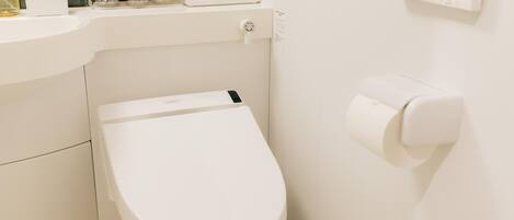 A modern bathroom with a white toilet, a sink with toiletries, and a paper towel dispenser.