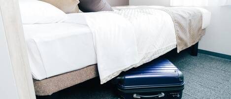 A bed with a white comforter and pillows, a blue suitcase on the floor, and a carpeted floor.