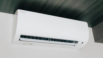 A white air conditioning unit mounted on a wall with a dark wooden ceiling.