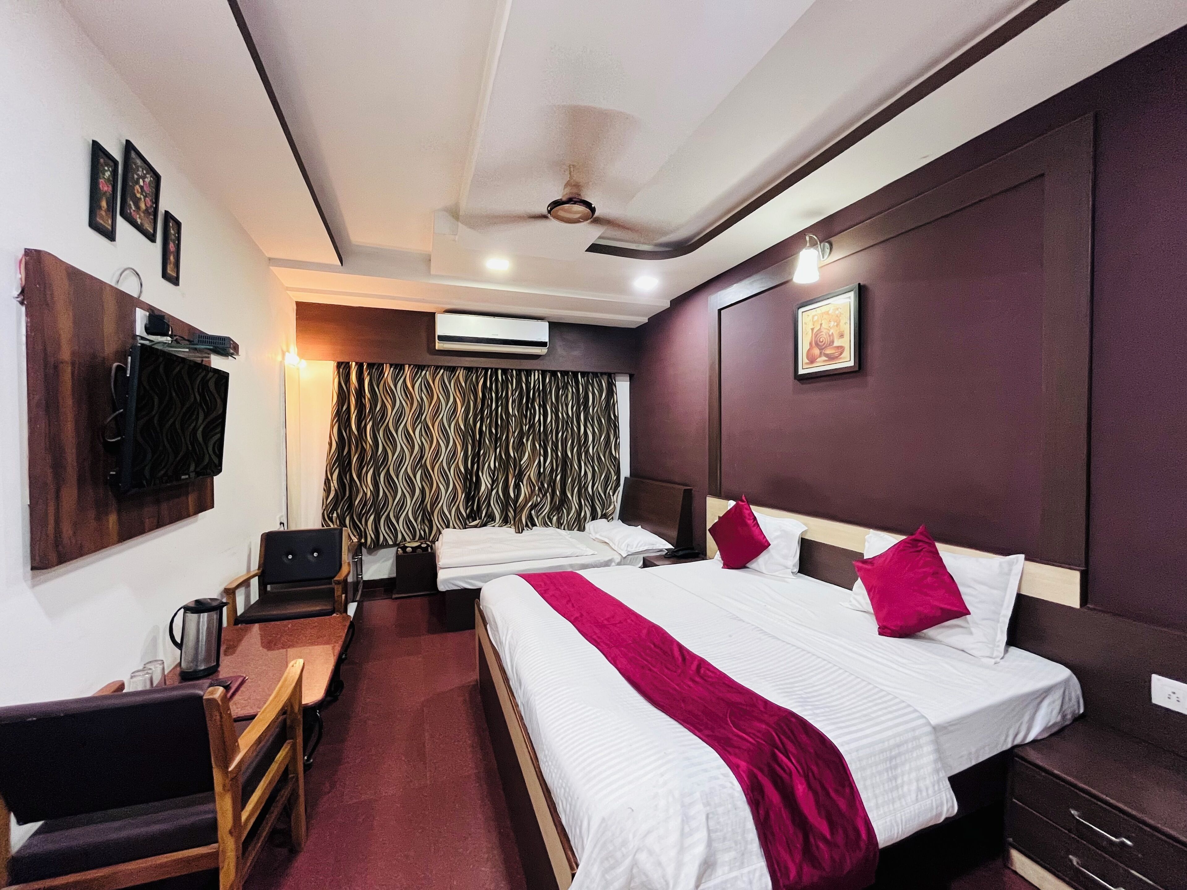 A hotel room with two beds, a desk, a chair, a TV, and an air conditioning unit.