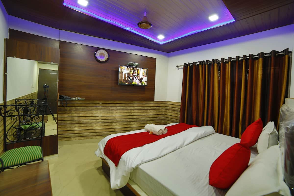 Une chambre d’hôtel avec une tête de lit en bois, un téléviseur fixé au mur, un lit avec une literie blanche et des oreillers rouges, et un plancher en bois.