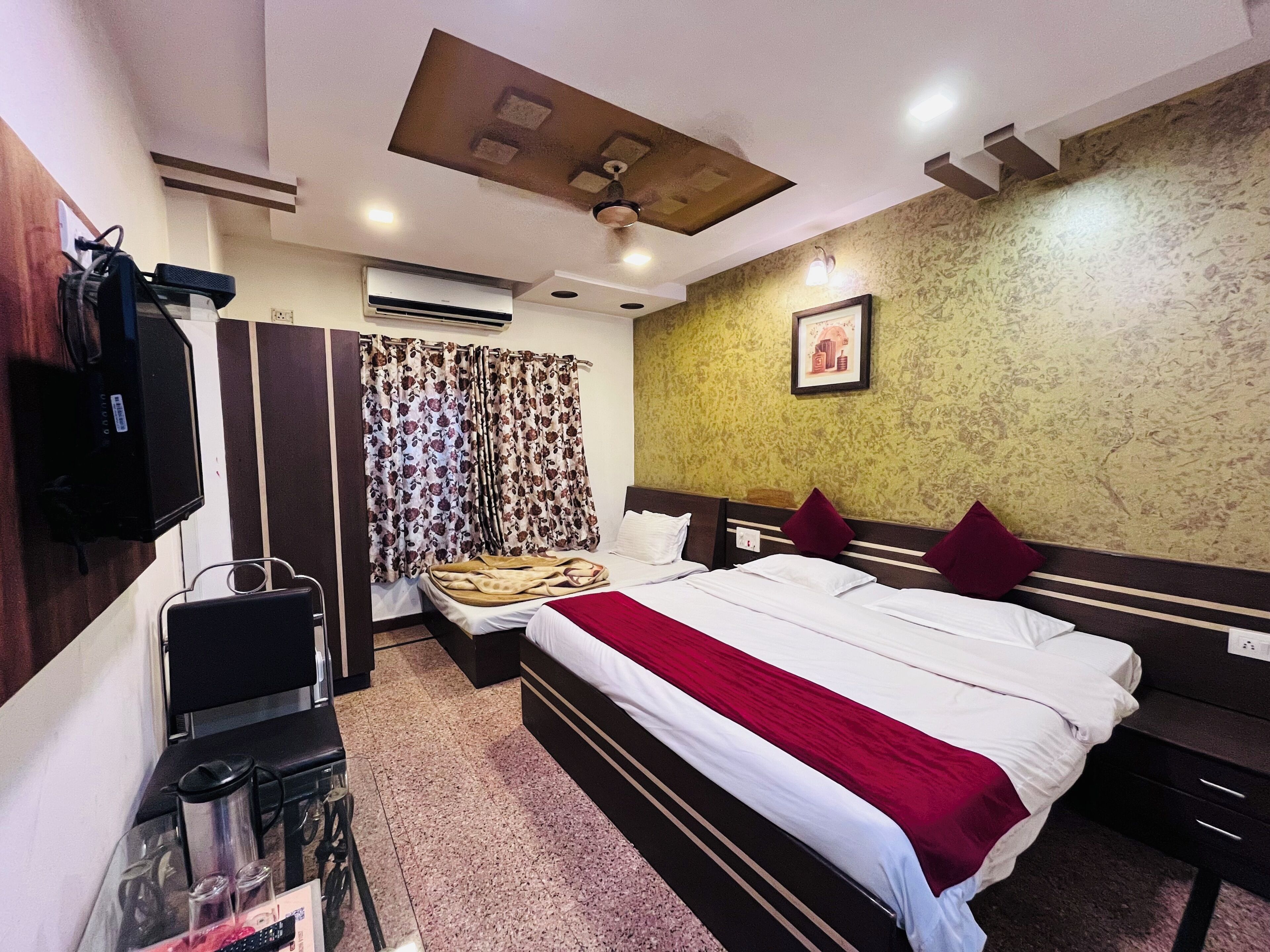 A hotel room with a bed, a desk, a television, an air conditioning unit, and a ceiling fan.