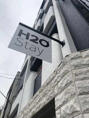 A sign indicating a hotel named "H2O Stay" with a modern architectural style featuring stone and concrete elements.