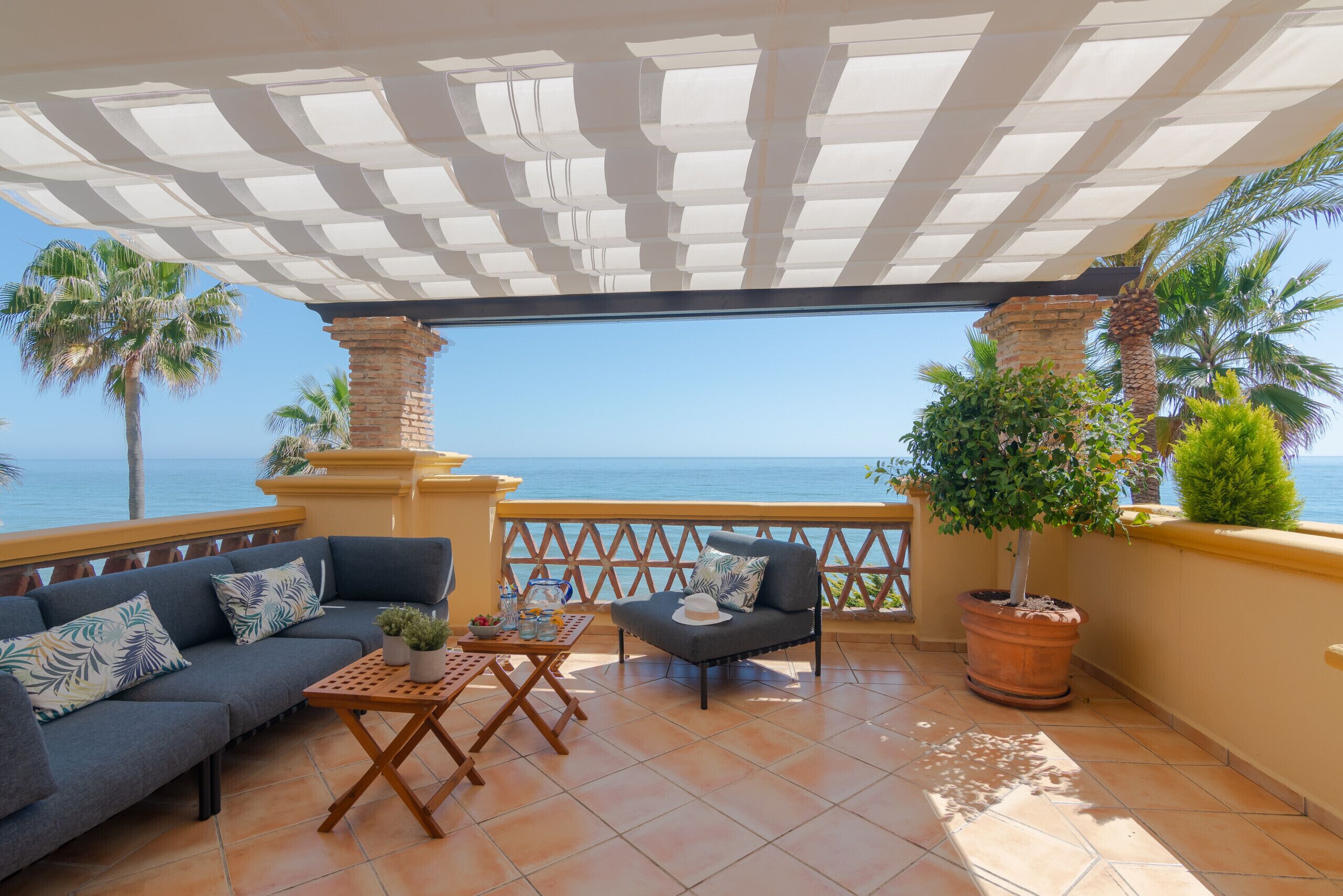 A terrace with a sofa, a chair, a table, and potted plants.