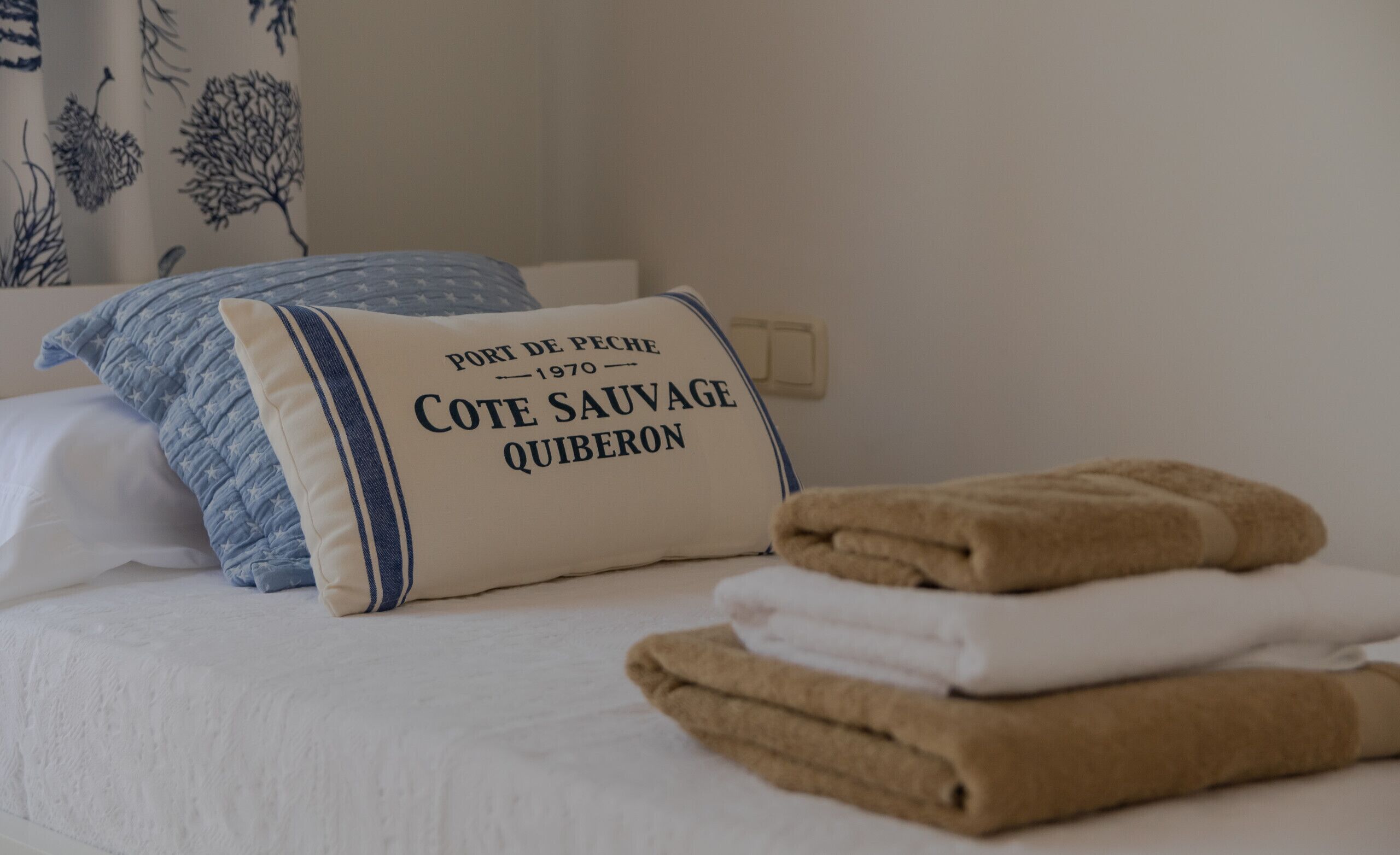 A bed with a pillow labeled 'Port de Peche 1970 - Cote Sauvage Quiberon' and folded towels.