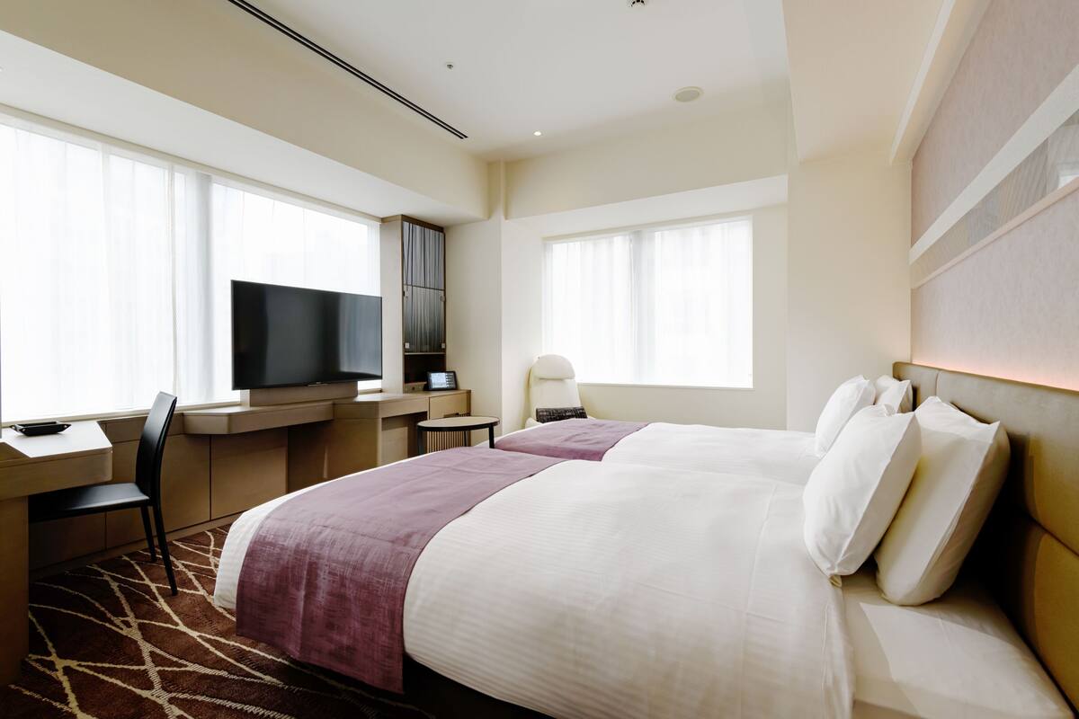 Habitación de hotel con una cama grande, un escritorio con computadora, televisión y una ventana con cortinas.