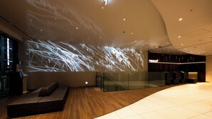 Un vestíbulo amplio con diseño moderno, que cuenta con una zona de estar espaciosa, una escalera de cristal y una proyección en la pared.