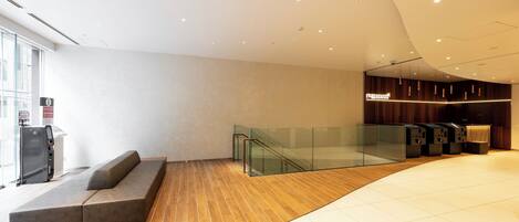 A modern lobby with a curved ceiling, a seating area with a sofa, a glass railing, and a reception desk.