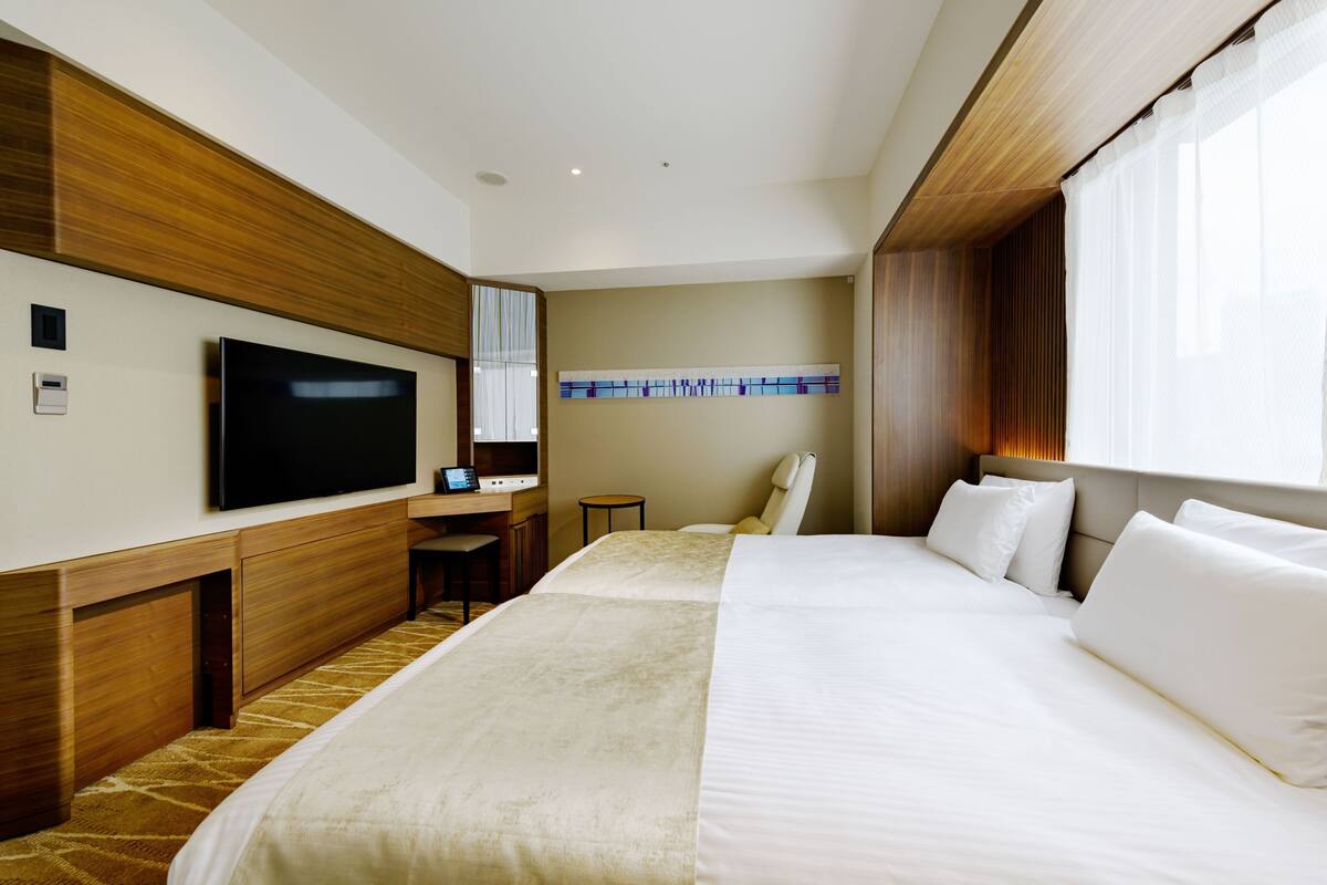 Habitación de hotel con una cama grande, un escritorio con una silla, un televisor y una ventana con cortinas.