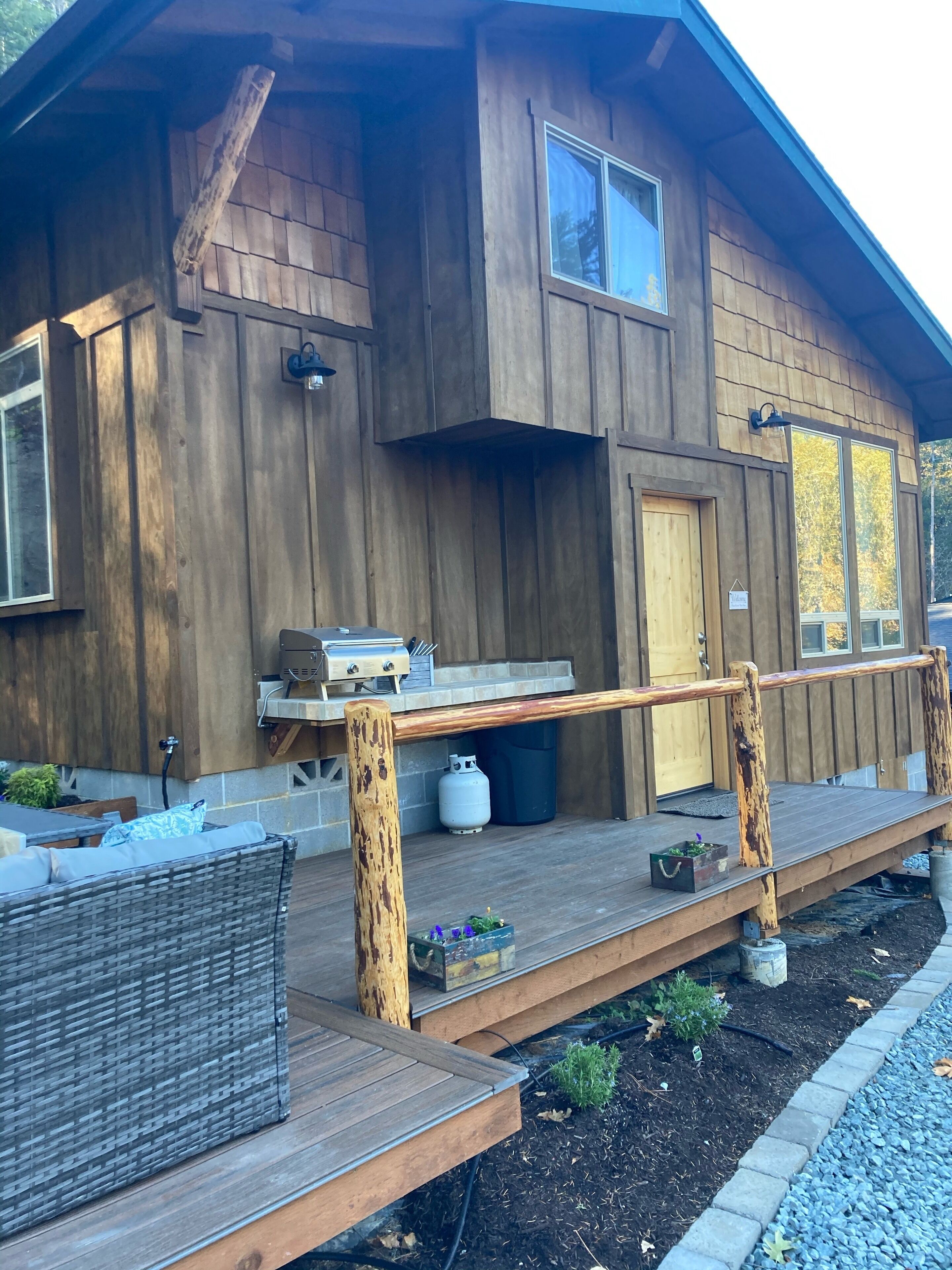 A wooden cabin with a porch, outdoor grill, and seating area.