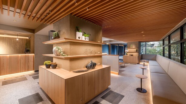 Een moderne receptie met een houten receptiebalie, inbouwkasten met planten en een zithoek met uitzicht op de omgeving.