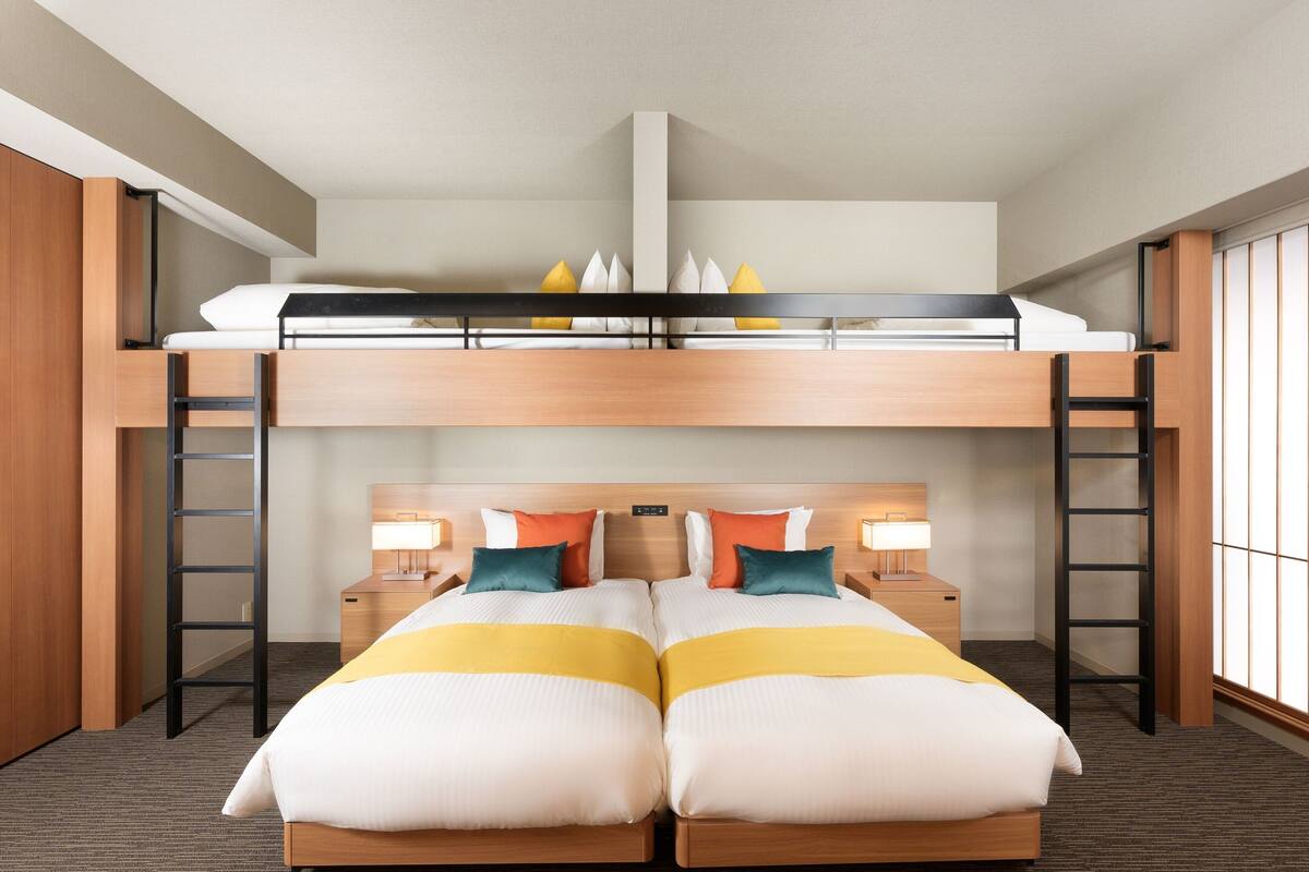Une chambre d’hôtel avec un lit superposé, deux tables de chevet avec des lampes et une vue sur l’extérieur grâce à de grandes fenêtres.