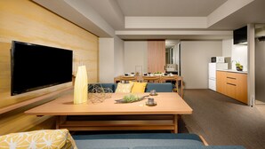 Een moderne hotelkamer met een houten eettafel, een blauwe bank en een flatscreen televisie die aan de muur hangt.