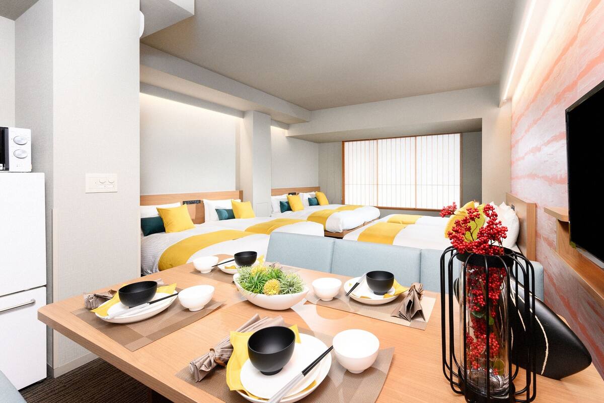 Une chambre d’hôtel avec un coin repas, deux lits avec une literie jaune et blanche, une télévision et une table de style japonais traditionnel, mise avec des bols et des baguettes.