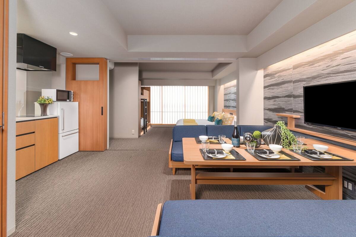Une chambre d’hôtel moderne équipée d’une kitchenette, d’un coin repas, d’une grande télévision et d’un lit.