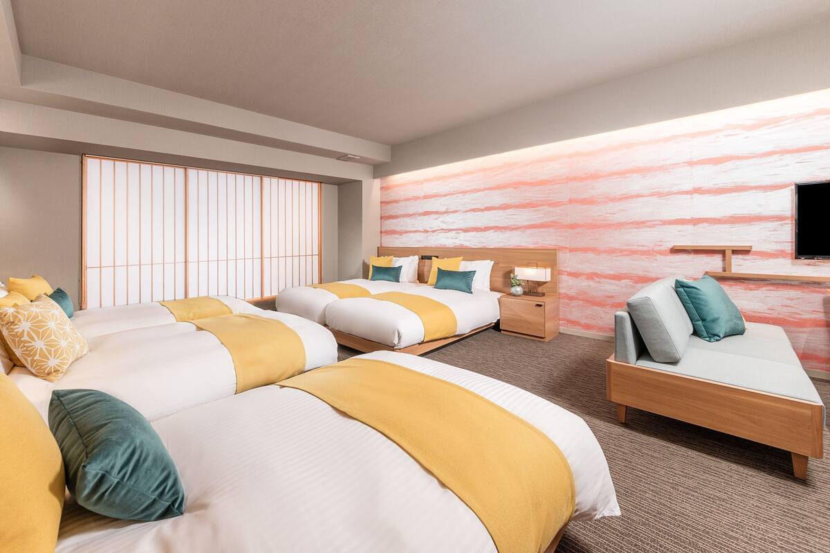 Une chambre d’hôtel avec deux lits, un canapé, une télévision et un paravent coulissant de style japonais.