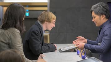 A group of people at a reception desk in a modern building with a marble floor and a dark wall in the background.