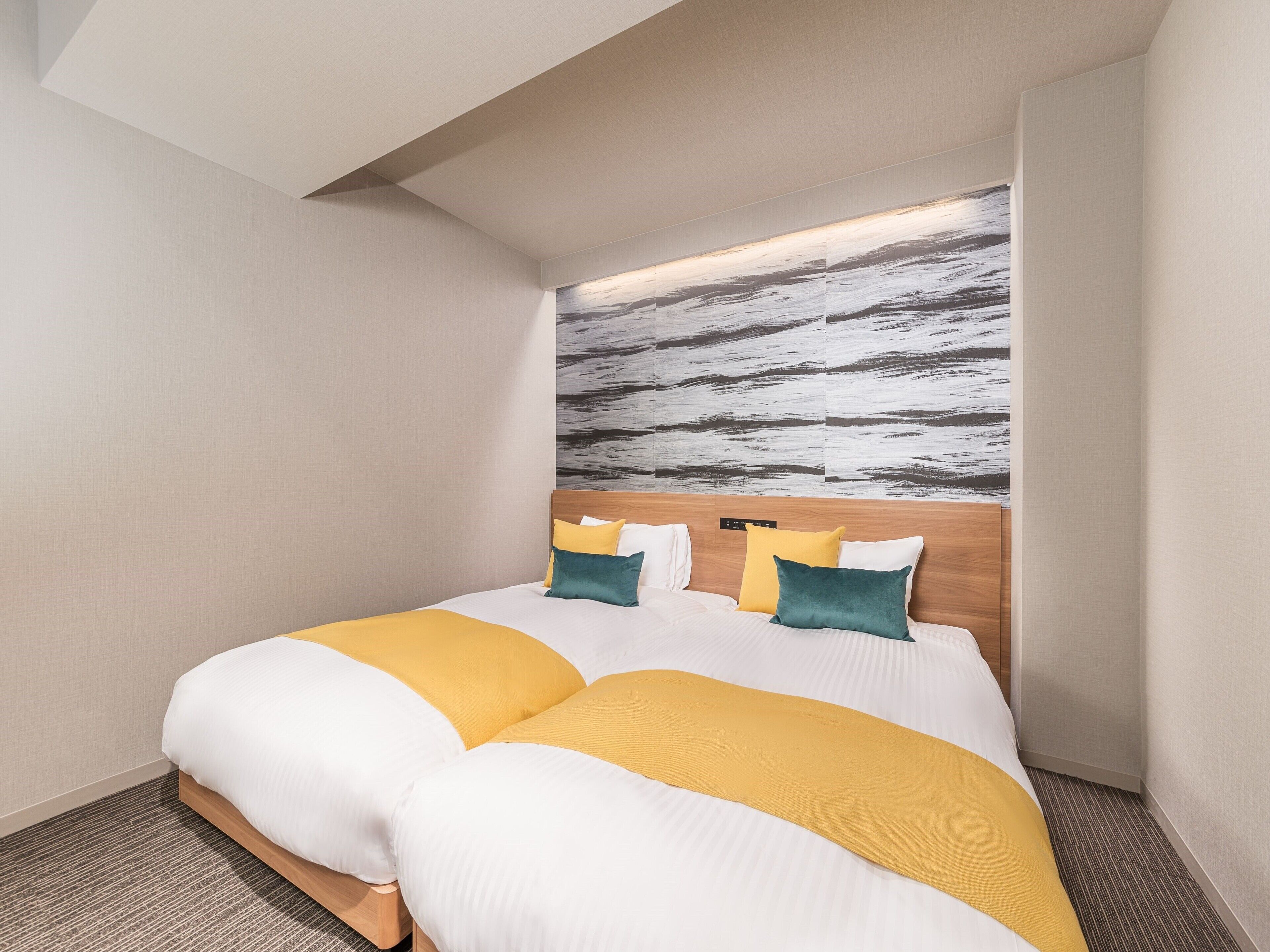 A modern hotel room with a large bed, a headboard with a control panel, and a textured wall art above the bed.
