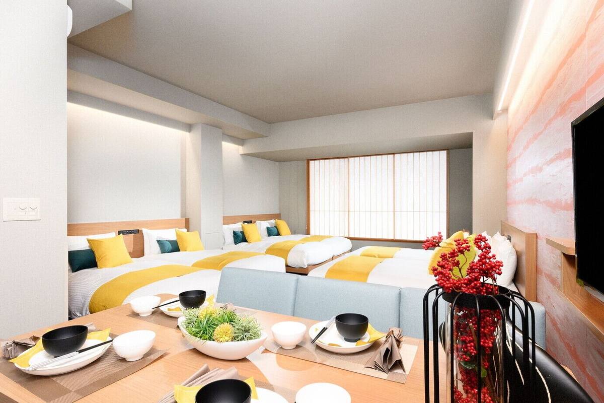 Une chambre d’hôtel avec deux lits, une table à manger avec de la vaisselle, une télévision et une fenêtre avec des stores.