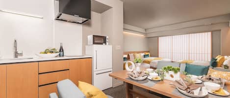 Una cocina moderna con microondas integrado, un lavamanos y armarios de madera. Hay una zona de comedor con una mesa para dos, un sofá y un ventanal con vistas.