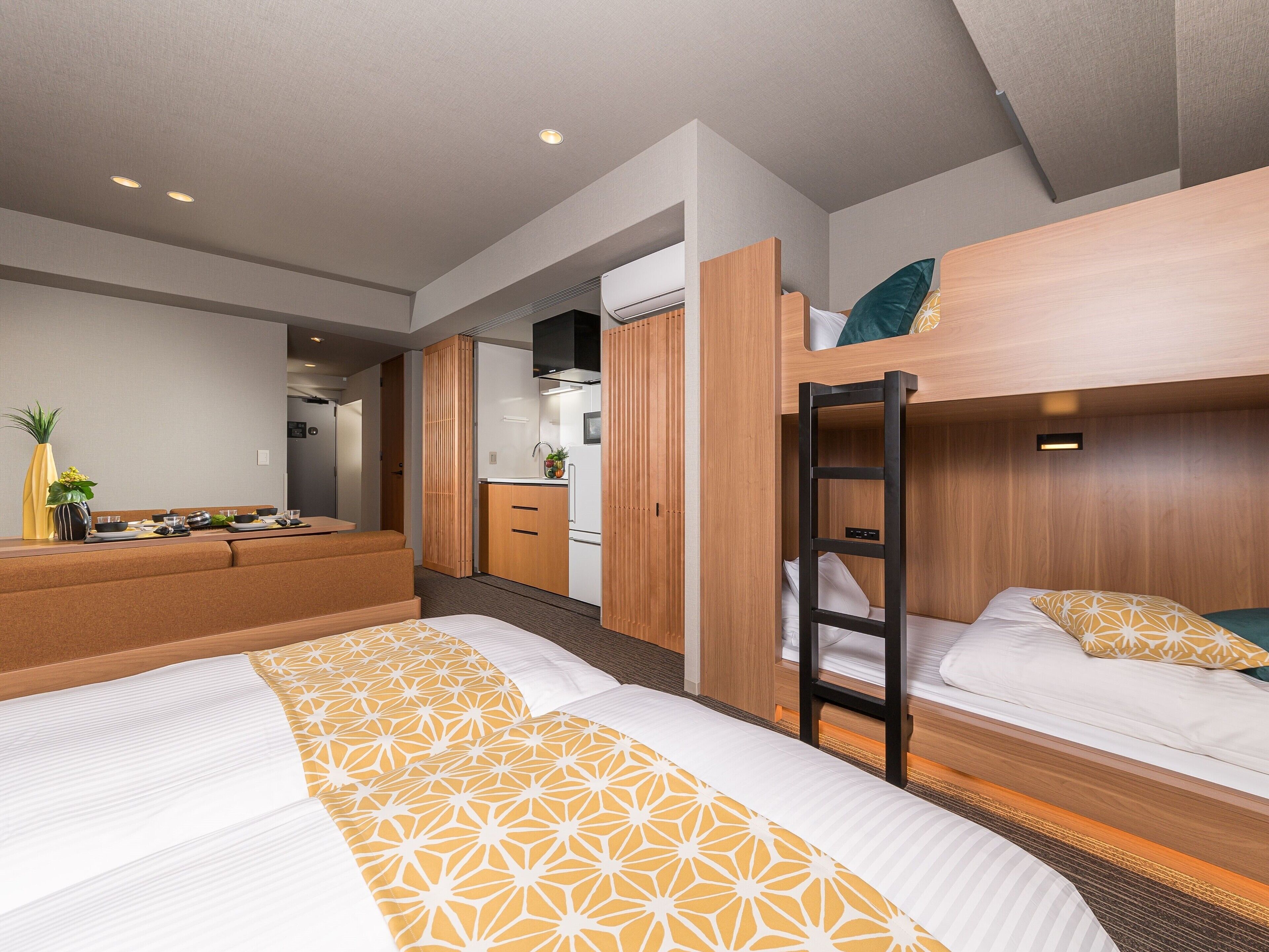 Quarto de hotel compacto com beliche, cozinha compacta e área de estar com mesa e cadeiras.