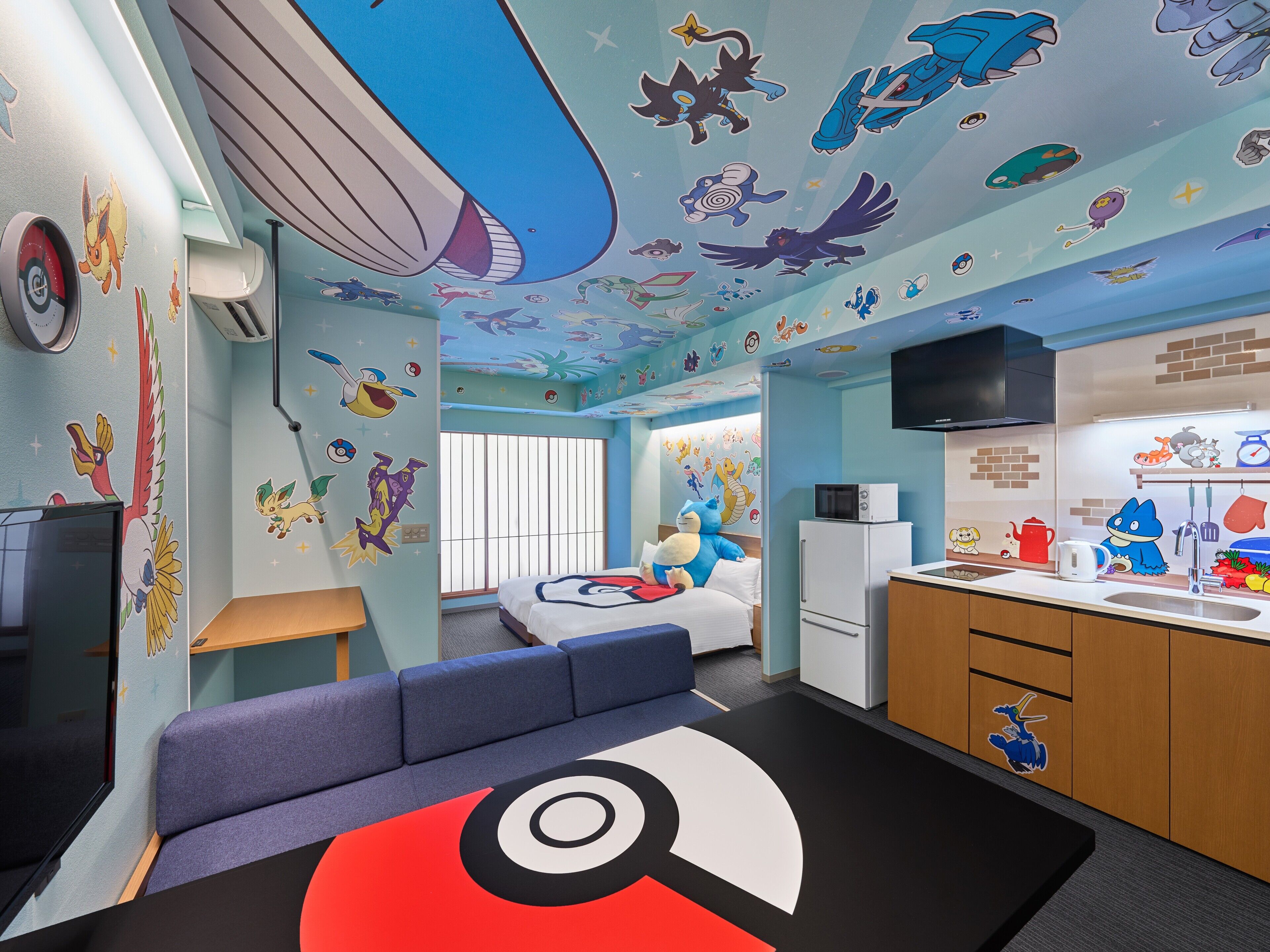 A room with a bed, a sofa, a kitchen area, and a ceiling with cartoon character decals.