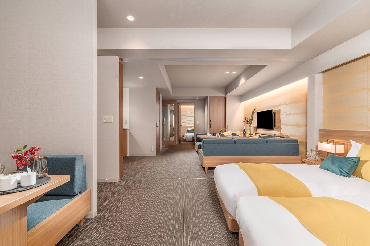 Une chambre d’hôtel moderne équipée d’un canapé, d’un lit, d’une télévision et d’un bureau agrémenté d’un vase de fleurs.