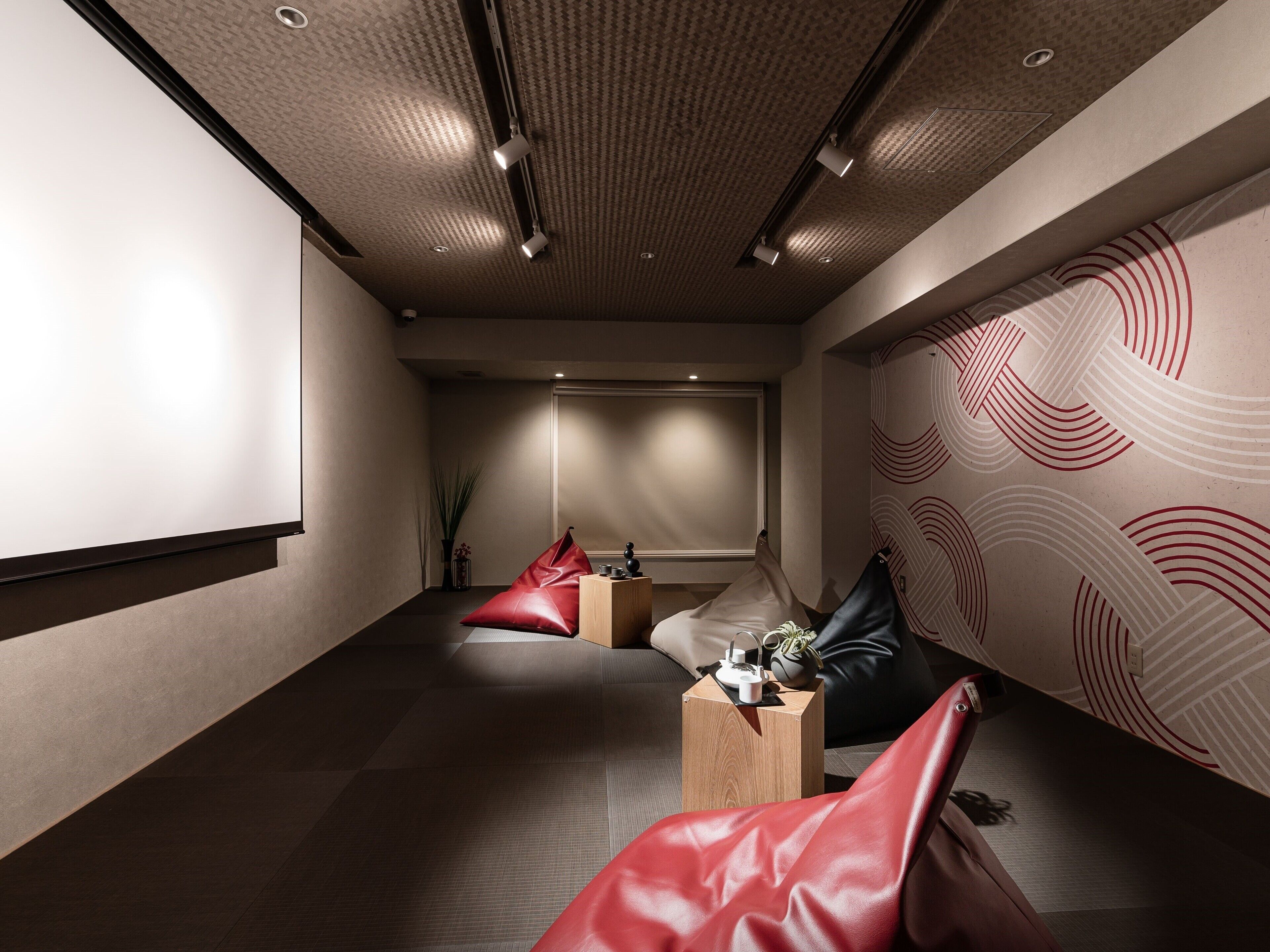 Une pièce moderne et bien éclairée, dotée d’un écran de projection, de sièges confortables et d’un mur orné de motifs.