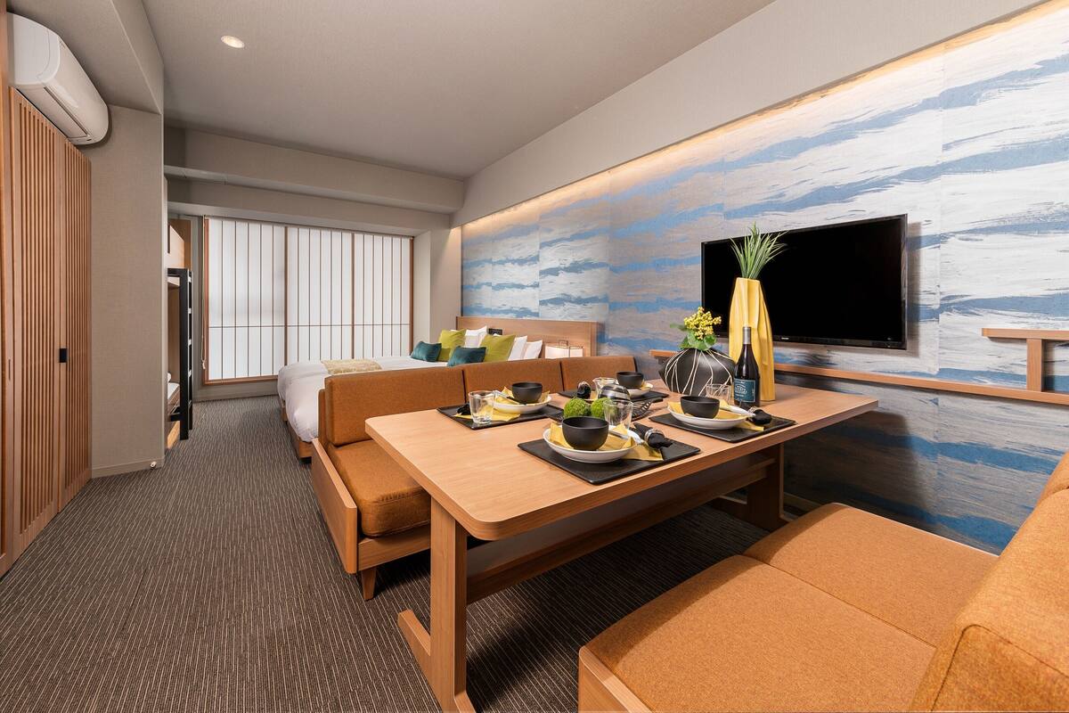 Une chambre d’hôtel moderne dotée d’un coin repas, d’un canapé, d’une télévision et d’un mur au décor texturé.